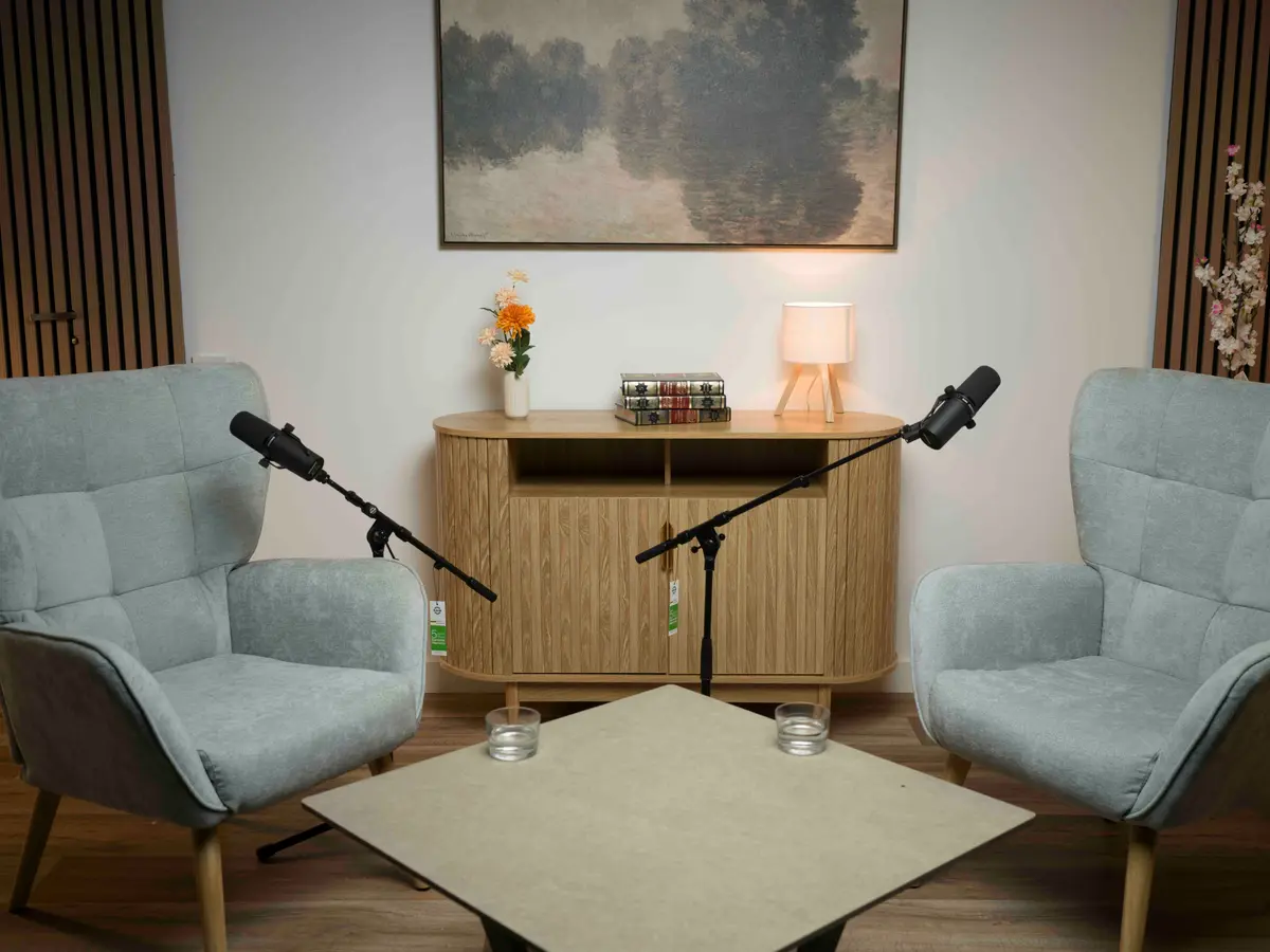 Sala blanca con dos sillones enfrentados, micrófonos y mesa baja